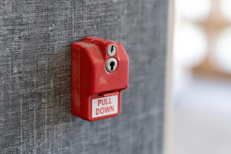Red fire alarm pull station mounted on textured grey fabric wall
