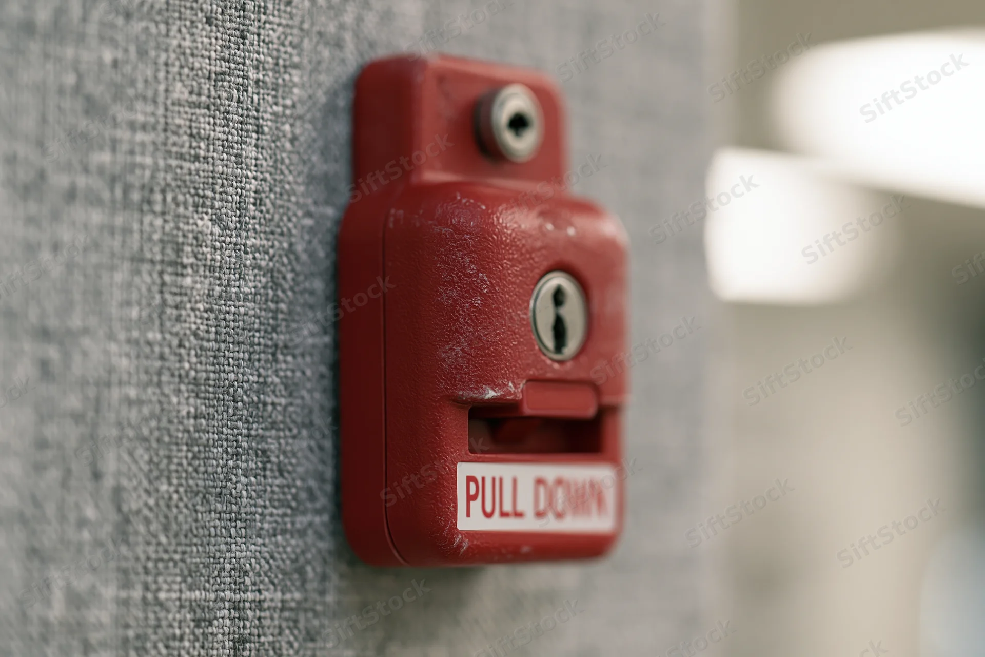 Red fire alarm pull station mounted on textured grey fabric wall
