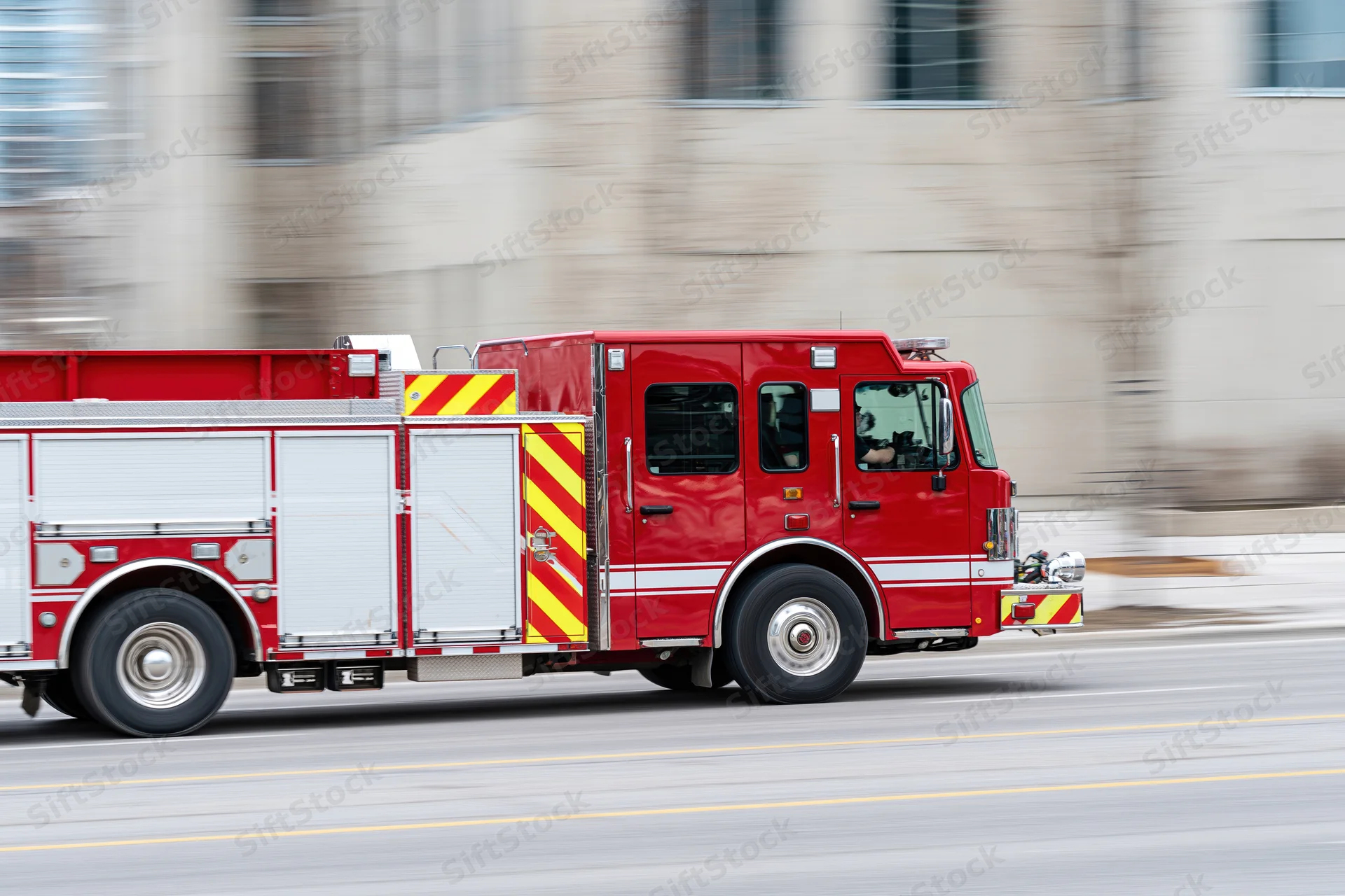 Red fire department engine truck speeding on city street with motion blur
