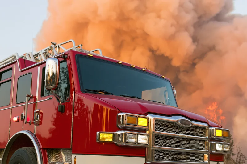Red firetruck viewed from low front-quarter angle with smoke and flames in background