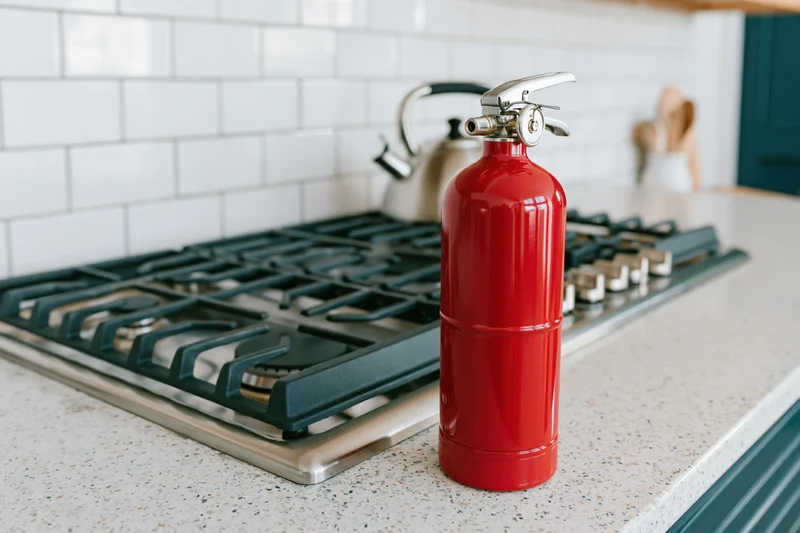 Red fire extinguisher standing on kitchen countertop beside gas stove