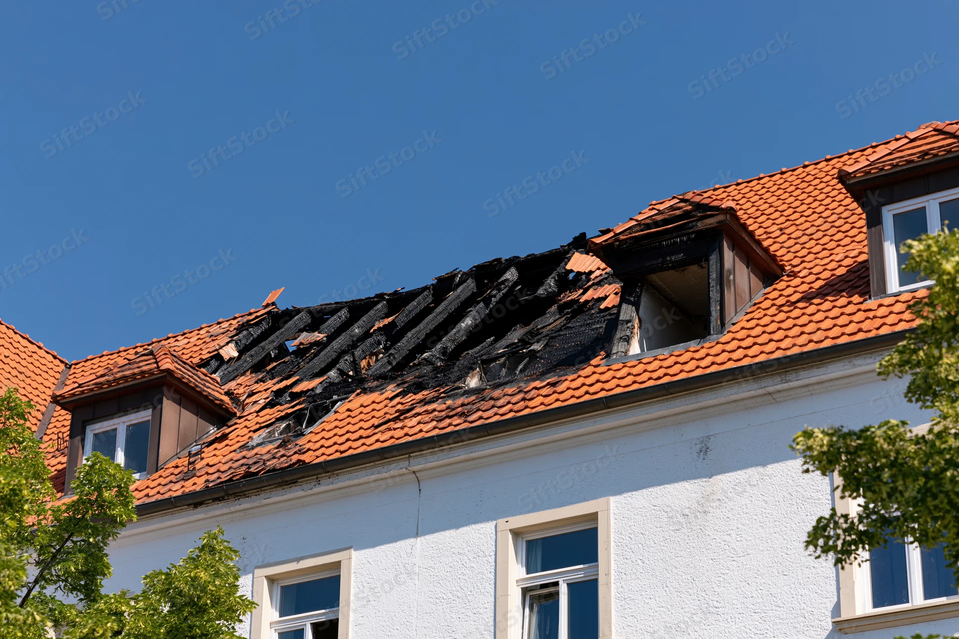 Fire-damaged roof on a residential apartment building under a clear blue sky