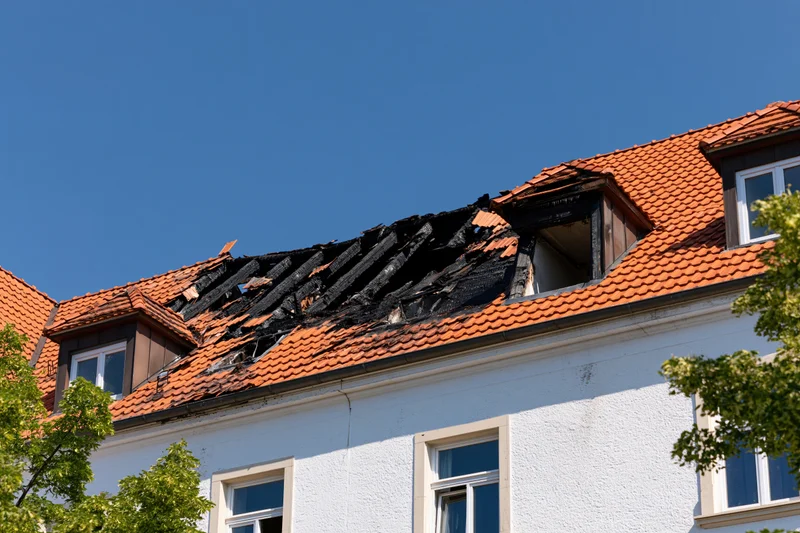 Fire-damaged roof on a residential apartment building under a clear blue sky