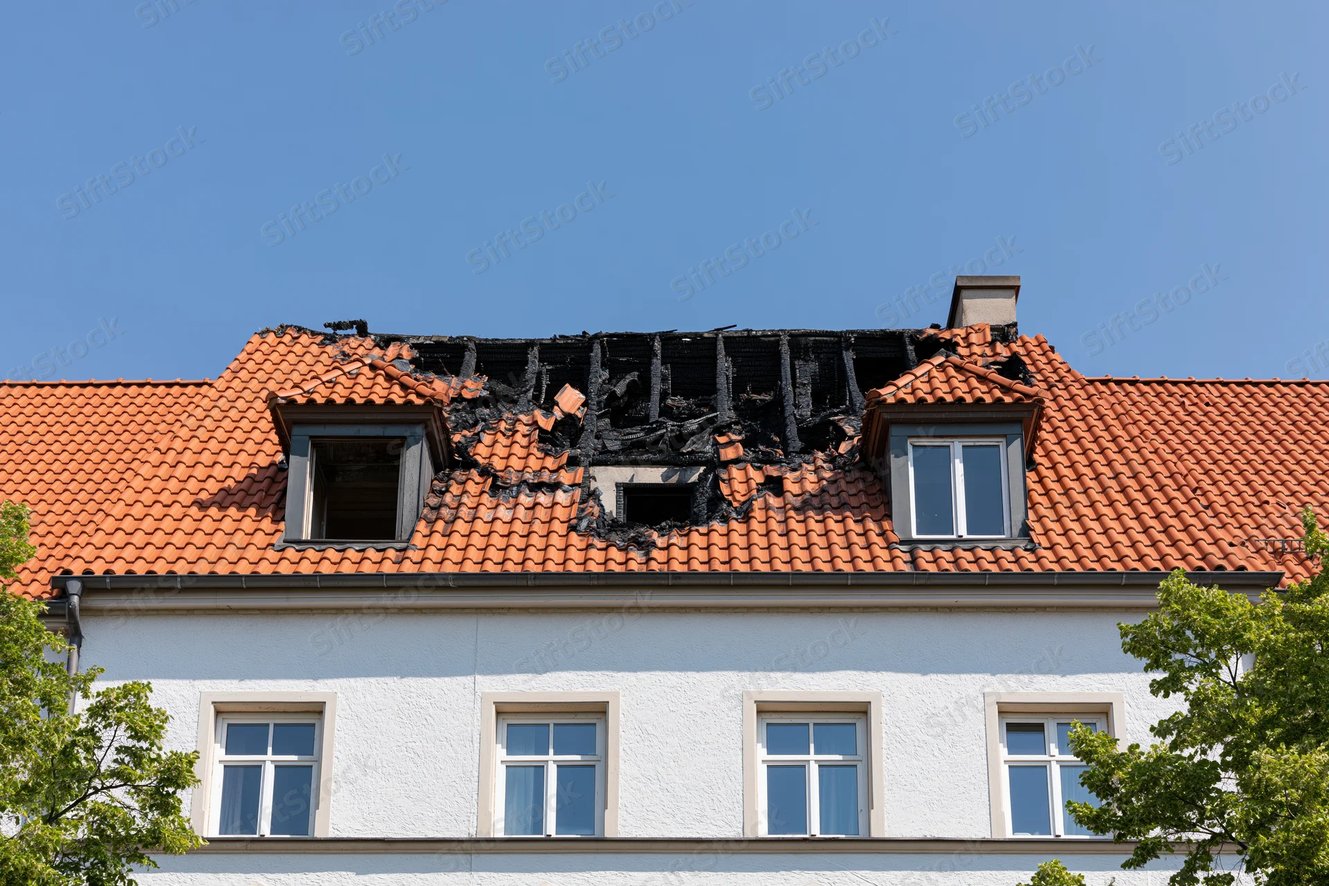 Fire-damaged roof of a residential european apartment building under clear blue sky