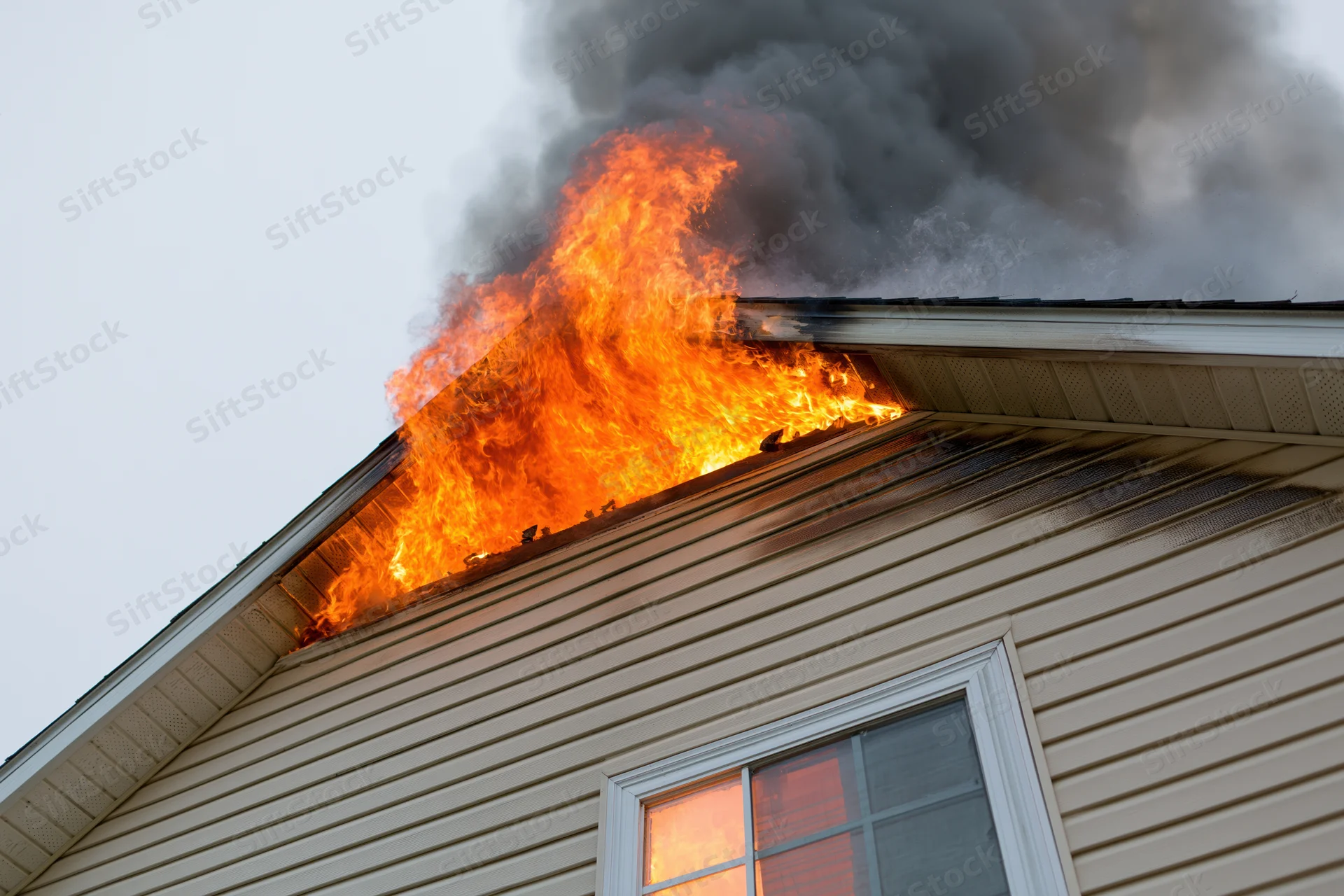 Flames erupting from roof of residential house with smoke billowing upward