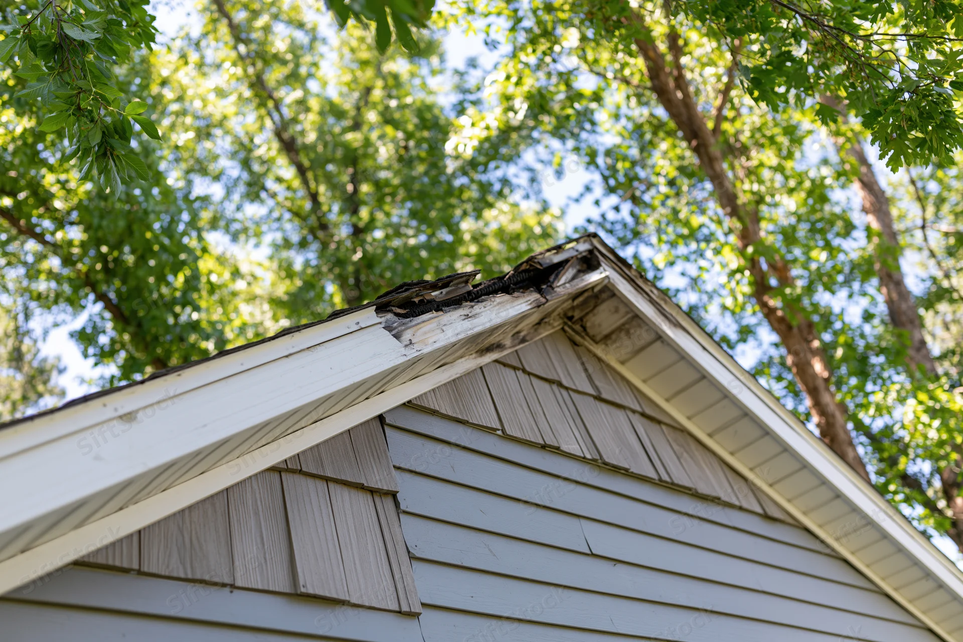 Damaged roof peak of a residential house with charred shingles and surrounding trees