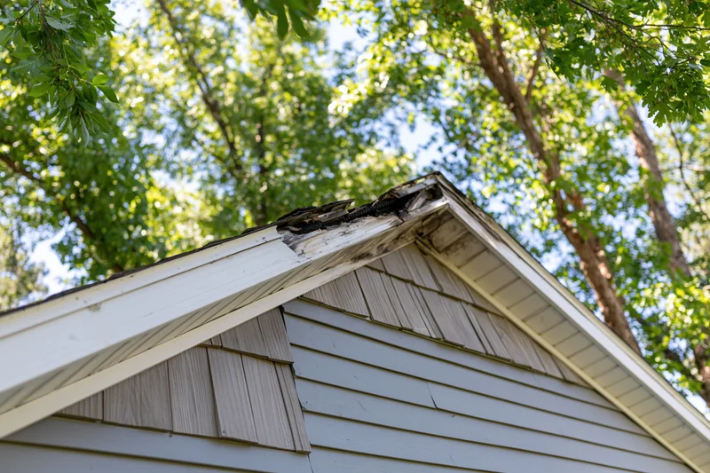 Damaged roof peak of a residential house with charred shingles and surrounding trees