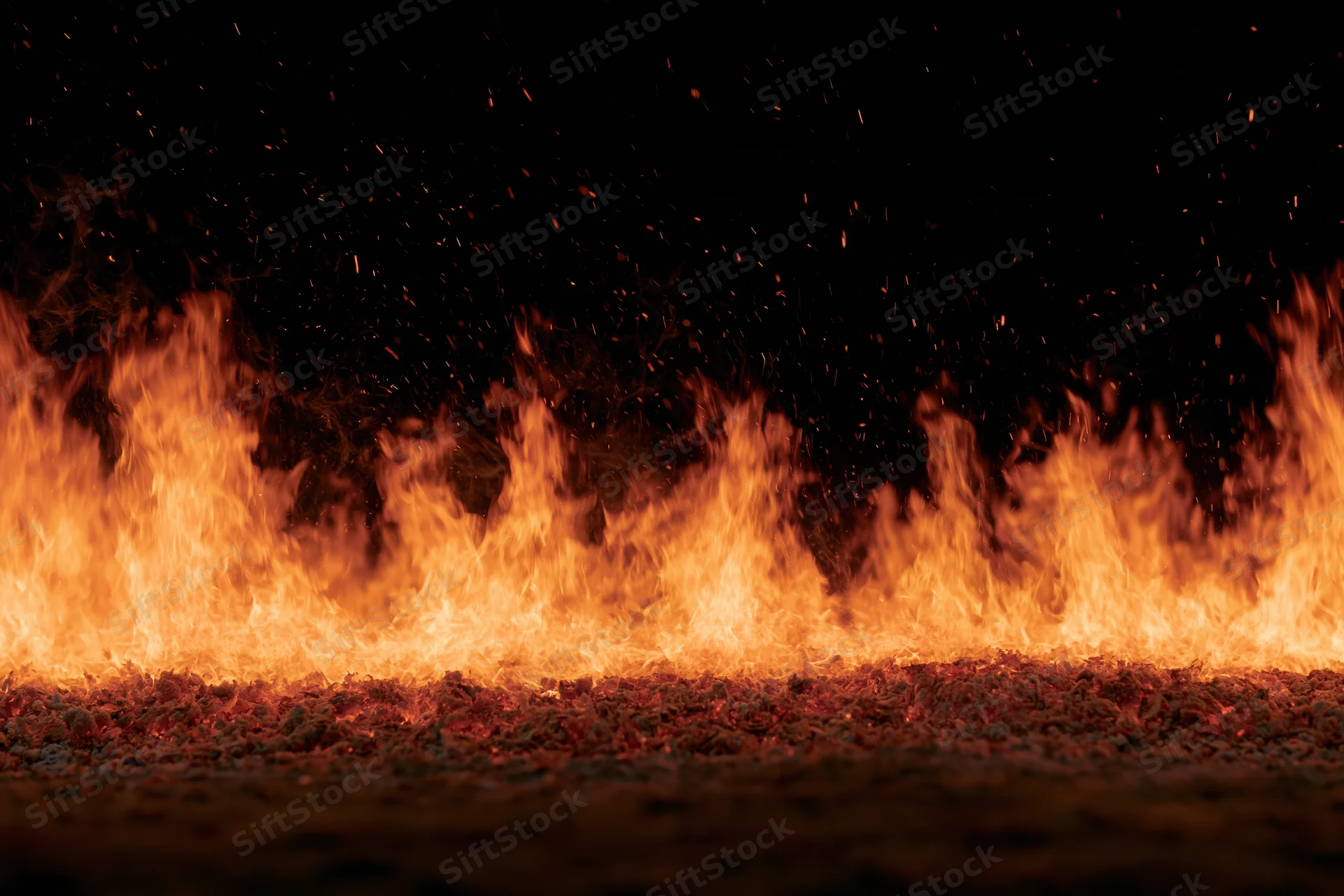 Row of intense flames burning across dark ground at night