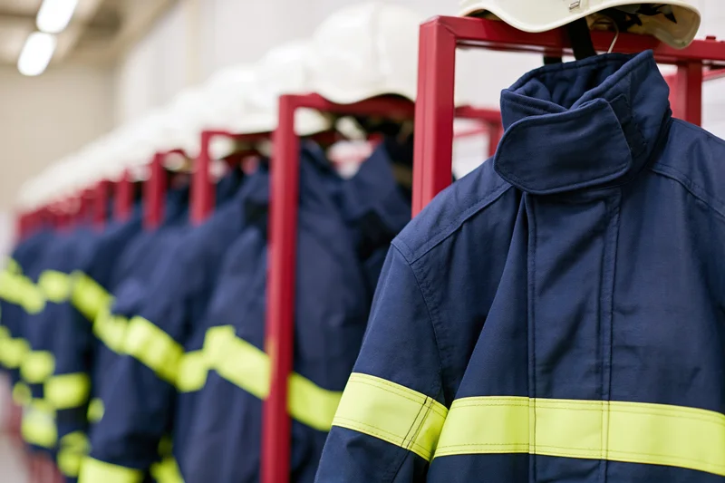 Navy blue firefighter turnout gear with yellow reflective stripes hanging on red metal racks in a fire station
