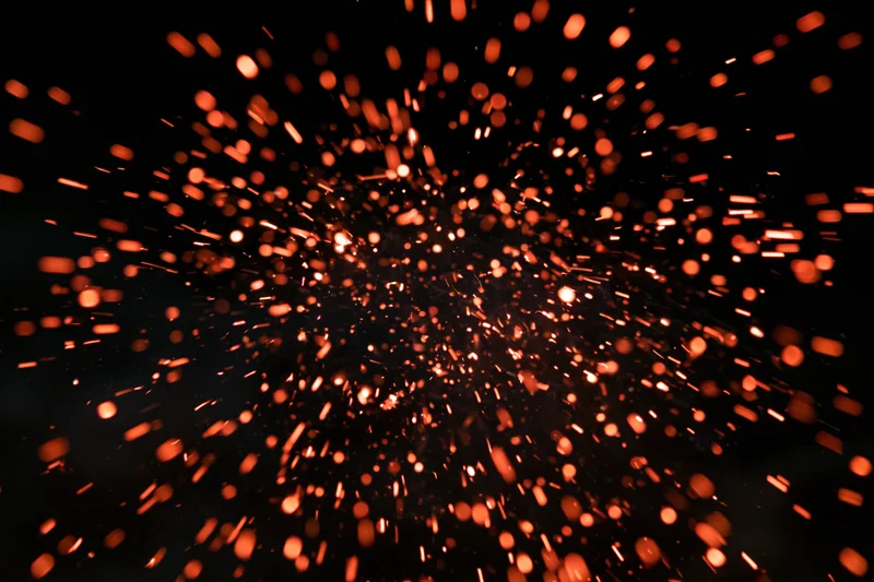 Glowing orange sparks bursting outward in dark night sky