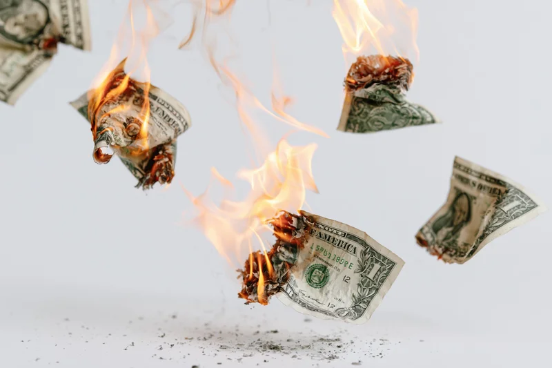 Burning one-dollar bills suspended in mid-air against a white background