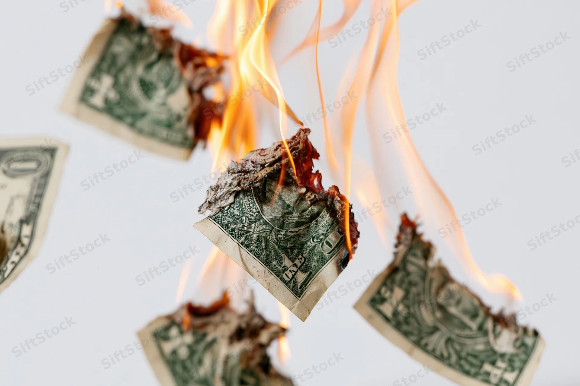Burning one-dollar bills suspended in mid-air against a white background