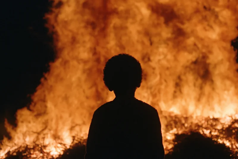 Silhouette of a child standing still facing a massive fire at night