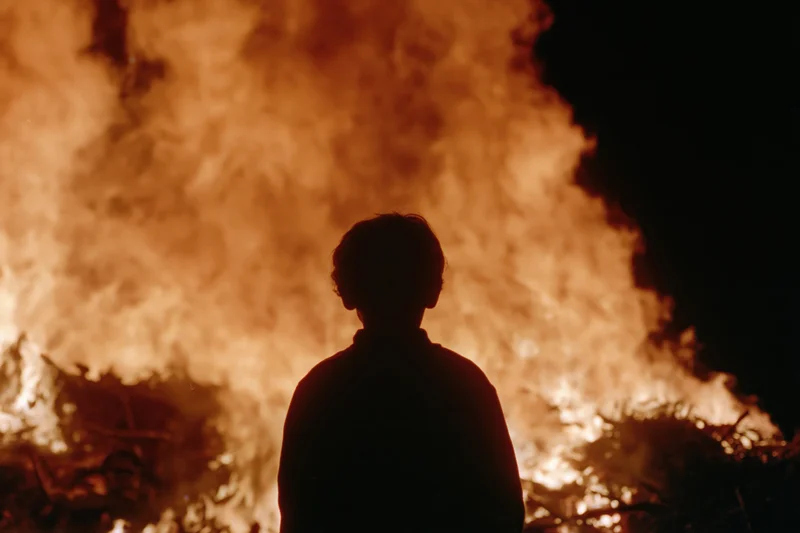 Silhouette of a child standing still facing a massive fire at night