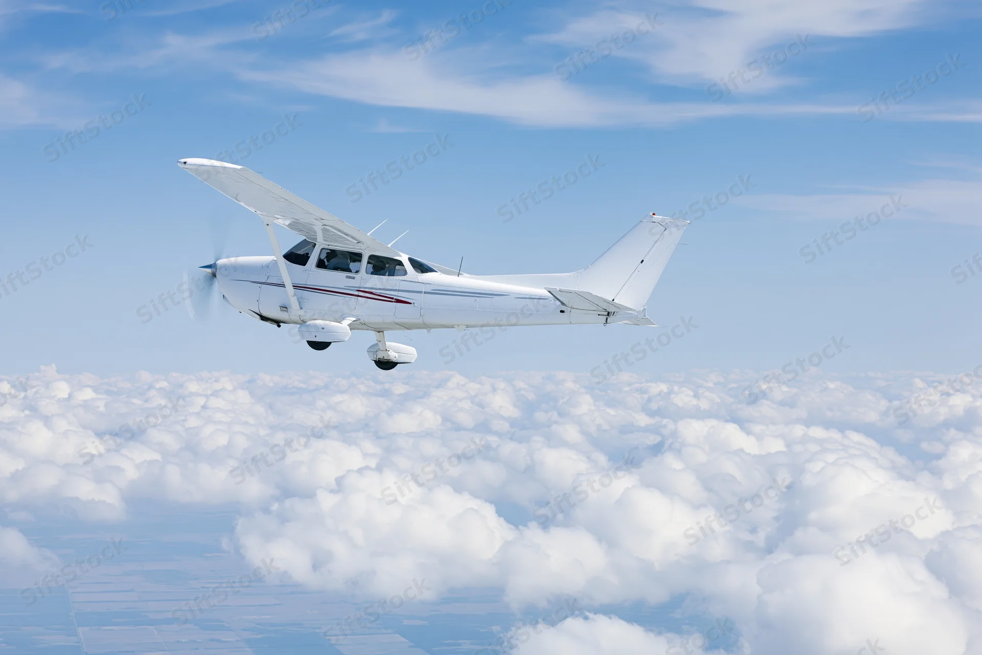 Small white single-engine propeller plane in level flight above clouds in blue sky