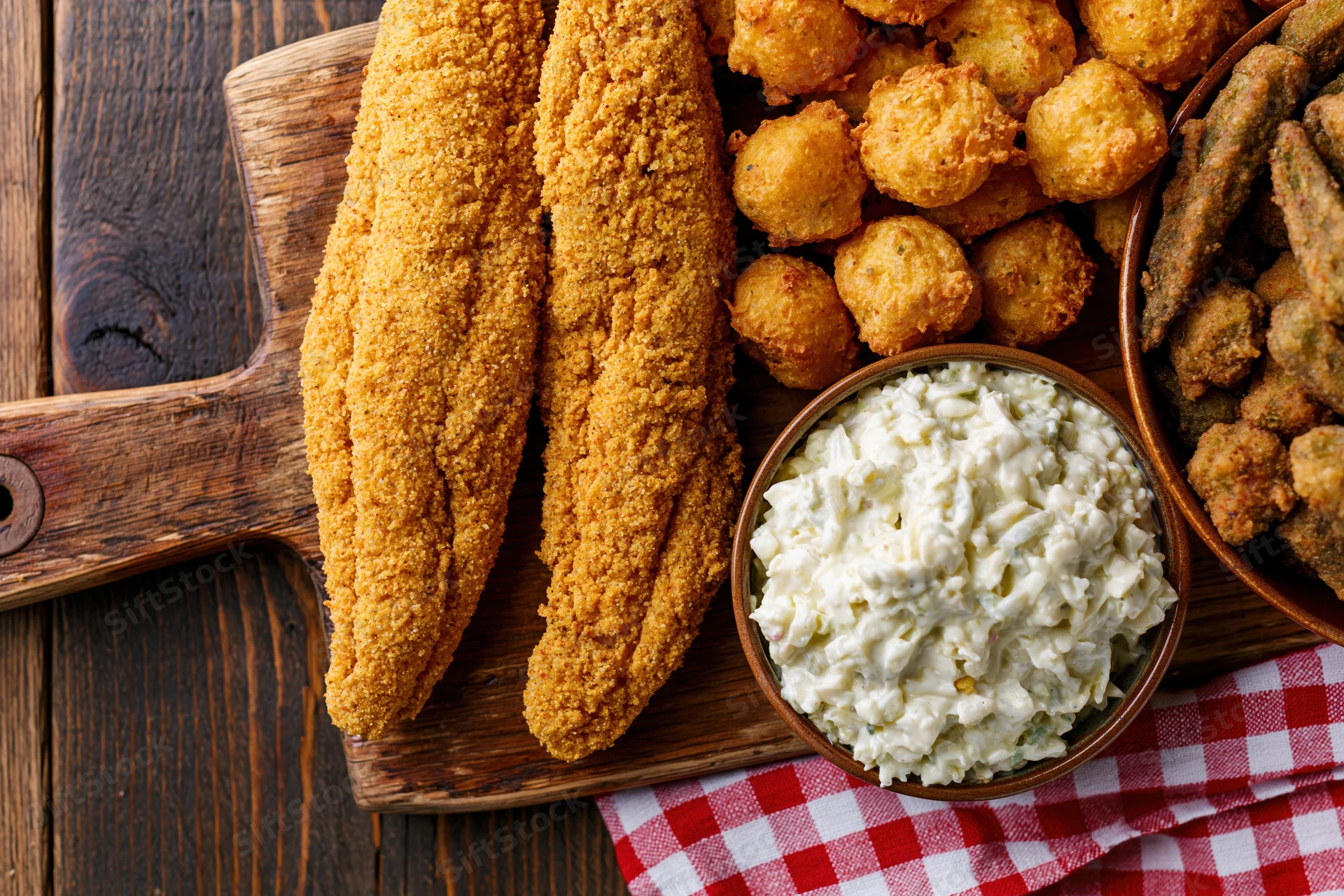 Fried fish and hushpuppies with coleslaw on a wooden board over a checkered cloth