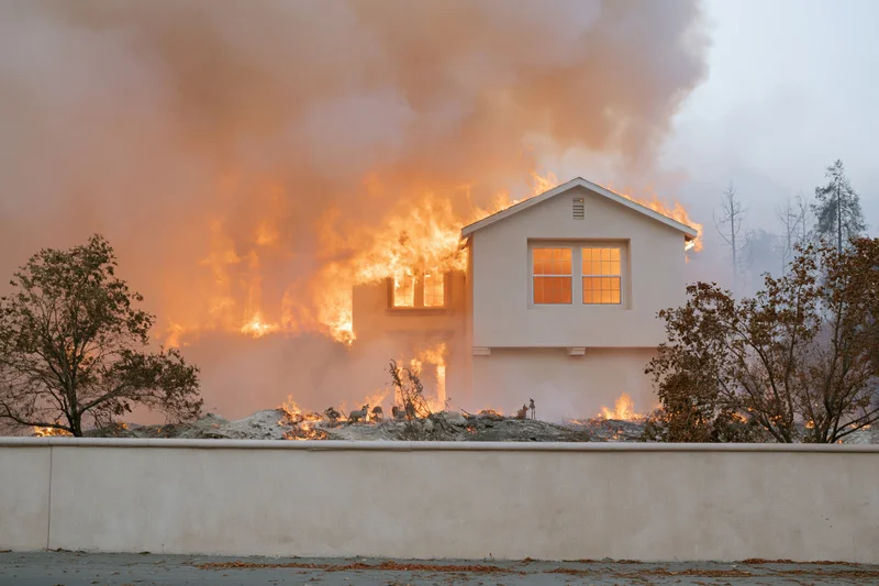 Suburban house burning with flames and smoke during wildfire