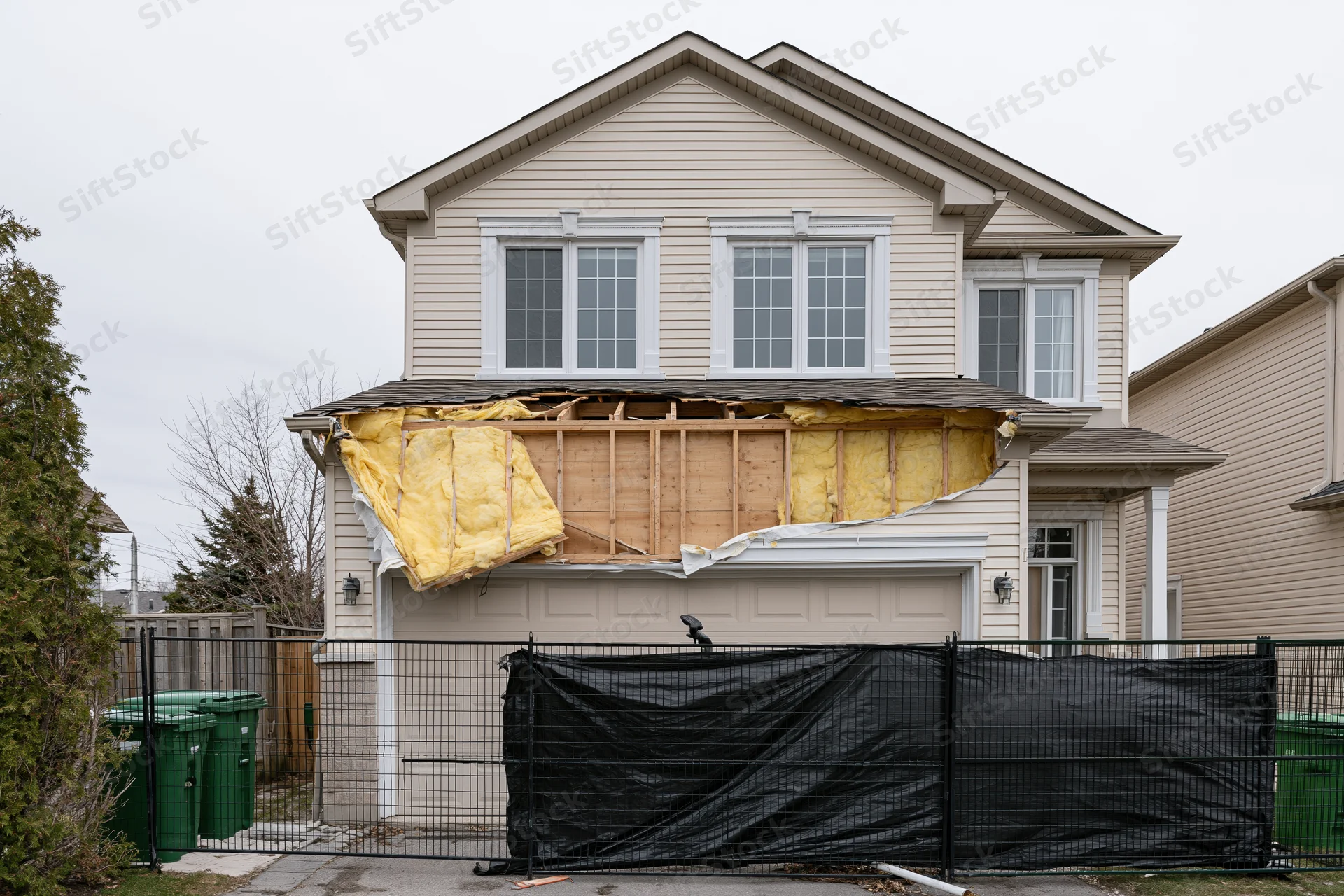 Two-story suburban house with exposed framing and insulation due to structural damage on front facade