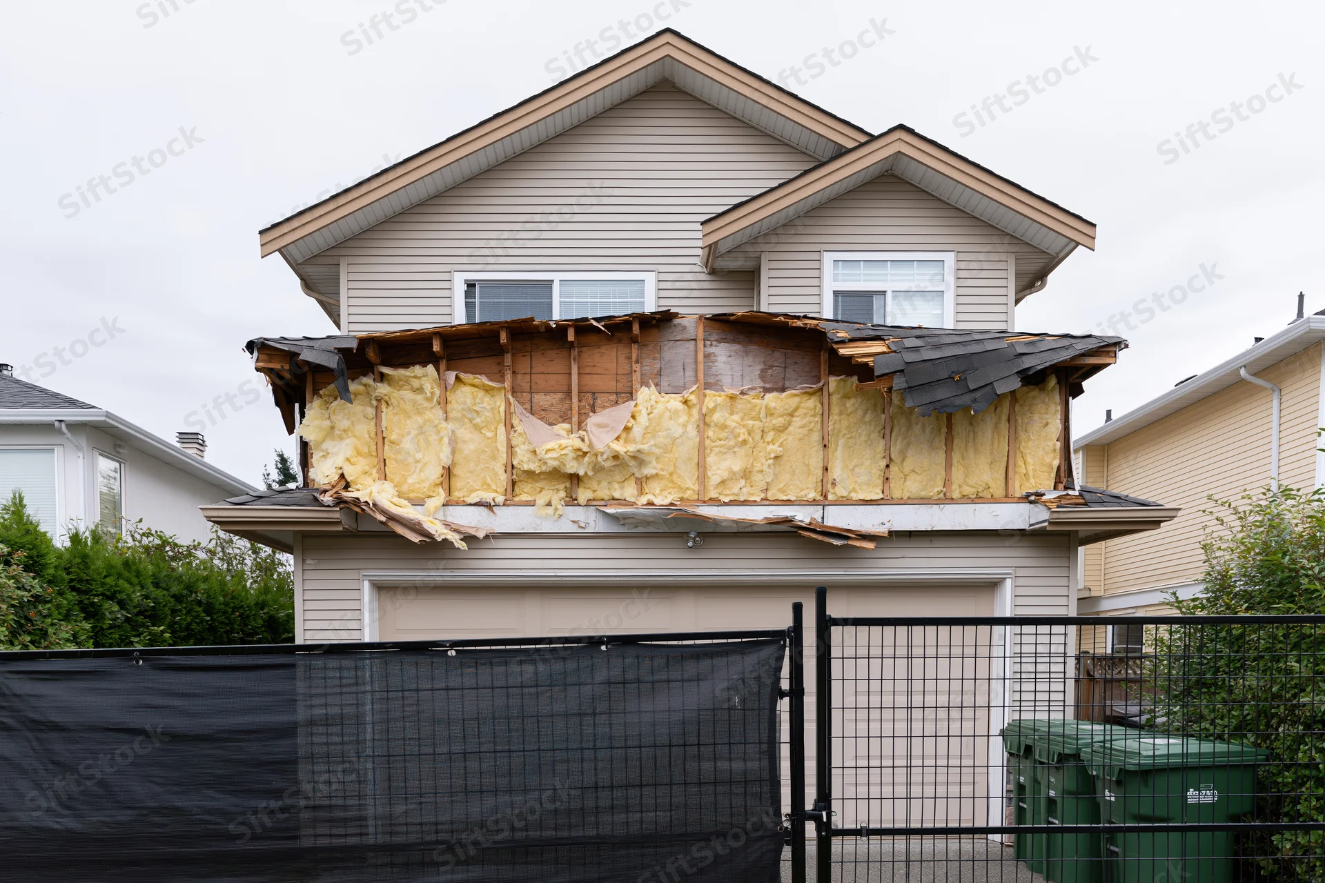 Two-story suburban house with exposed insulation and damaged roof above garage