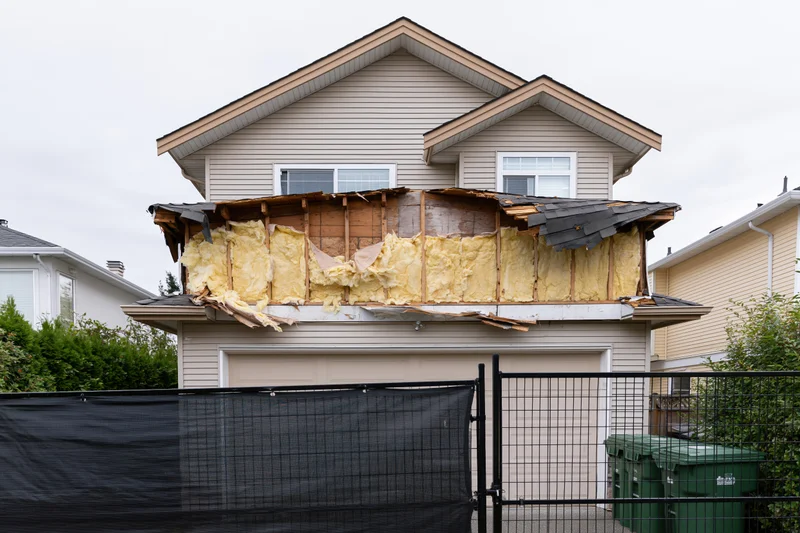 Two-story suburban house with exposed insulation and damaged roof above garage