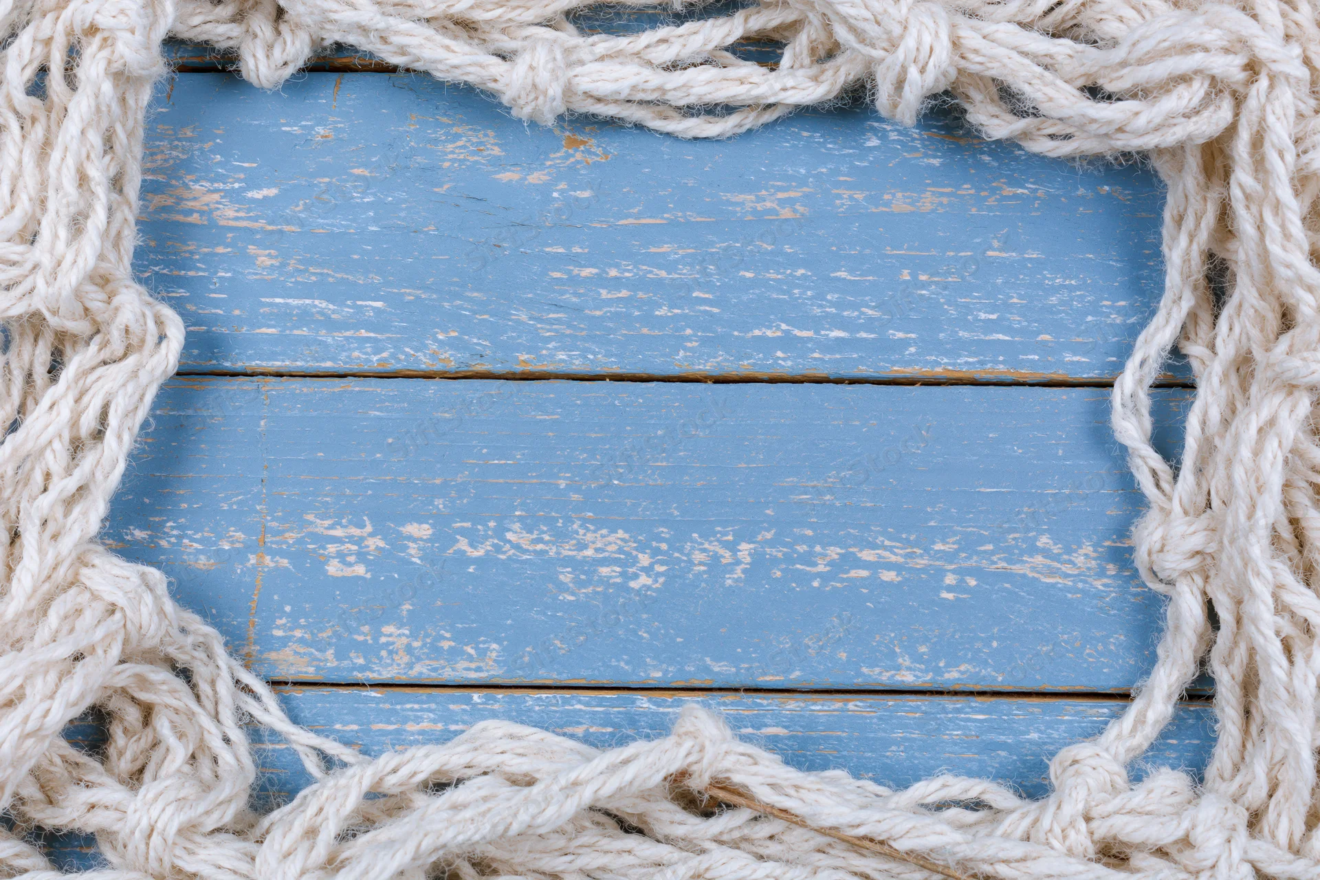 White fishing net cord arranged as a loose border frame on blue weathered wooden planks