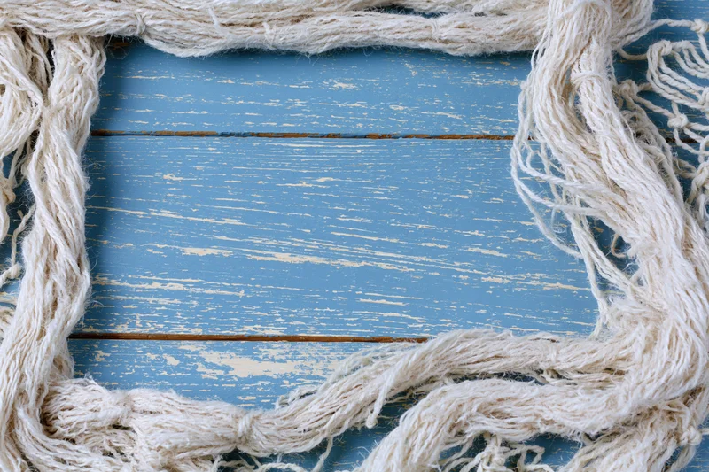 Tangled white fishing net cord arranged as a loose border frame on weathered blue wooden surface