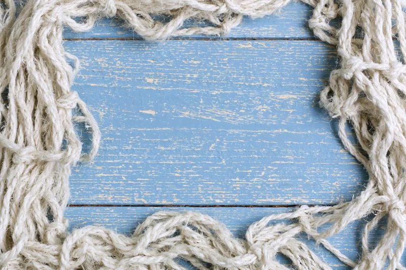 Tangled white fishing net cord arranged as loose border on blue weathered wooden surface