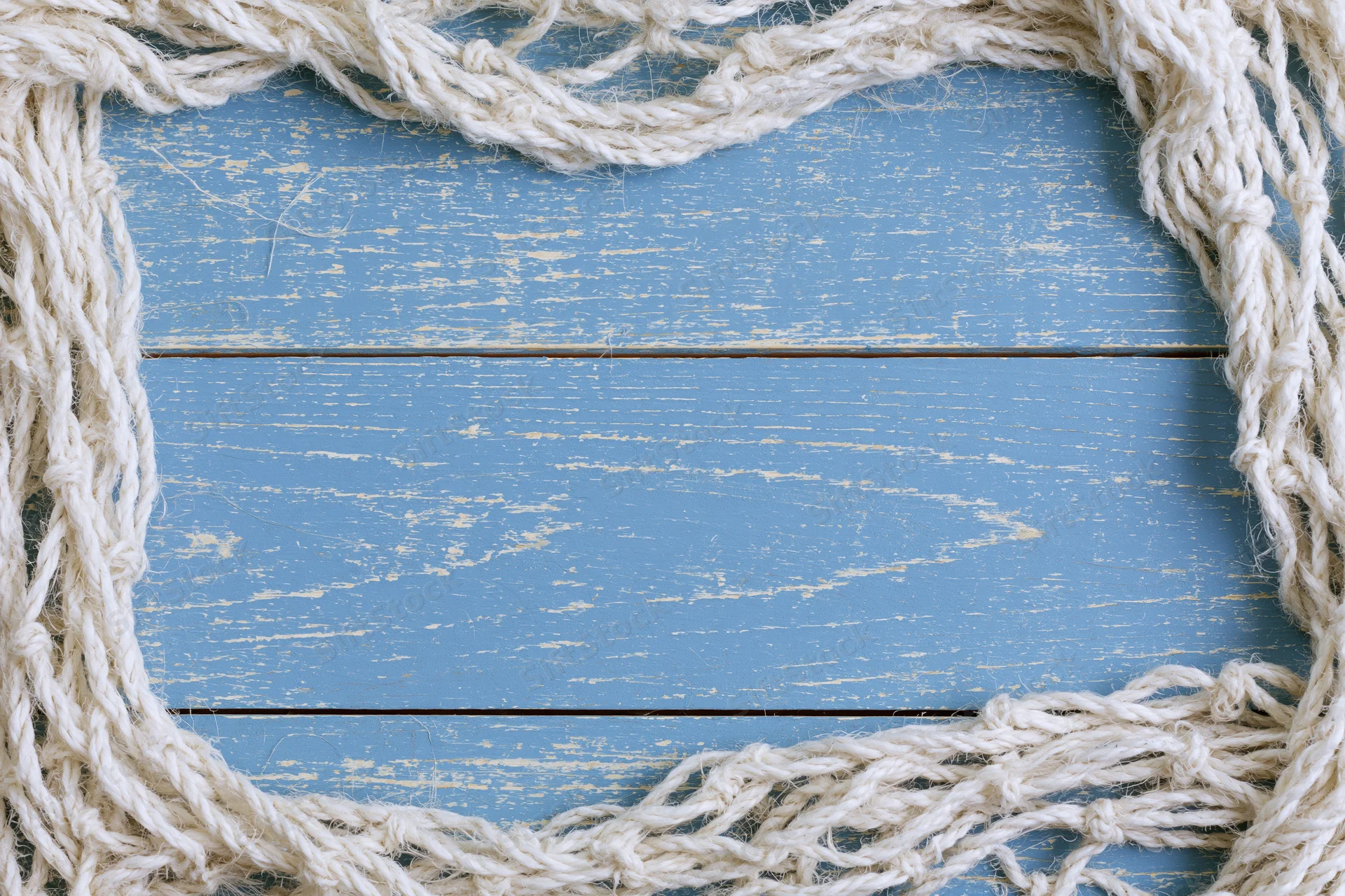 Tangled white fishing net cord arranged as loose border on blue weathered wooden surface