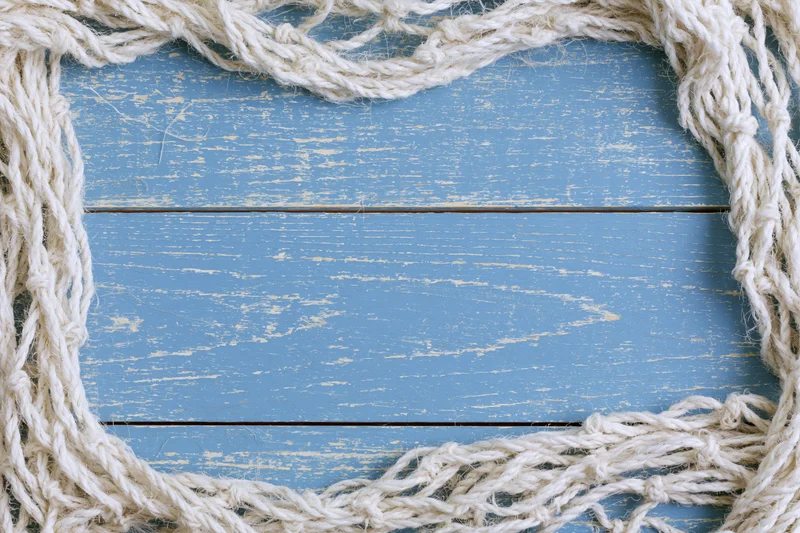 Tangled white fishing net cord arranged as loose border on blue weathered wooden surface