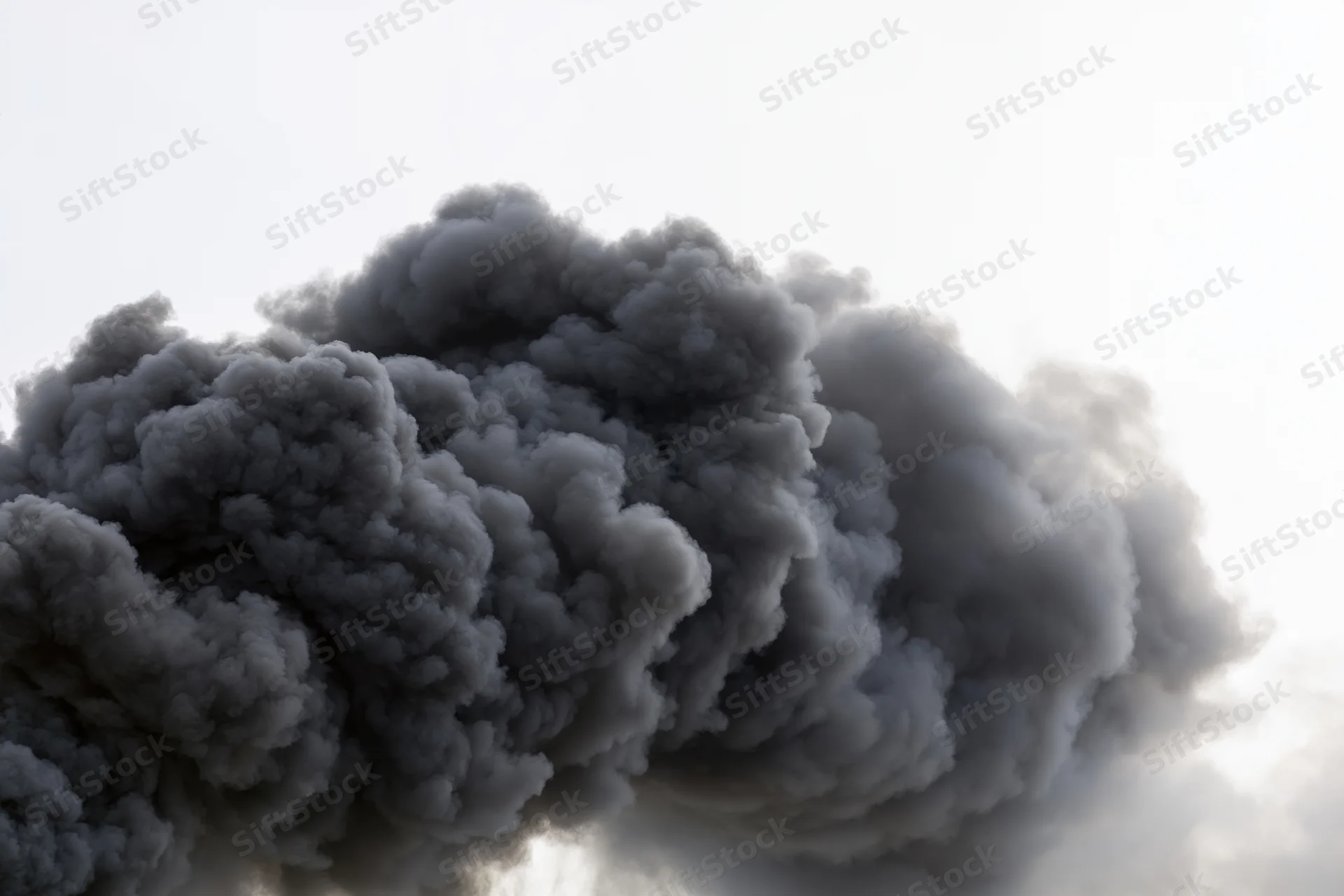 Thick black smoke rising in a turbulent plume against a pale sky