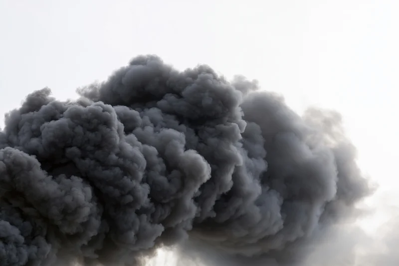 Thick black smoke rising in a turbulent plume against a pale sky