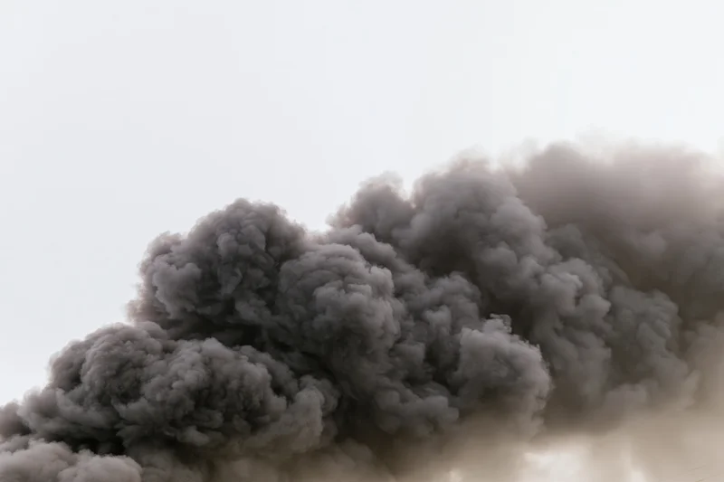 Thick gray smoke rising in a turbulent column against a pale sky
