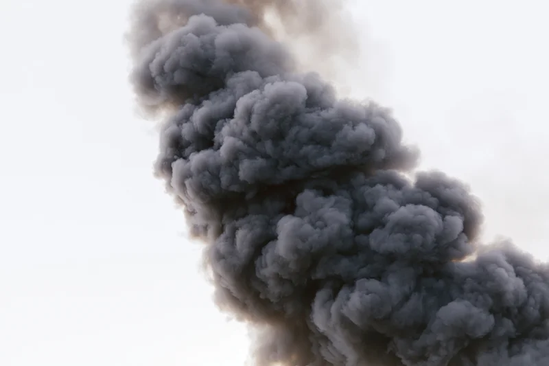 Thick dark smoke rising in a turbulent column against a white sky