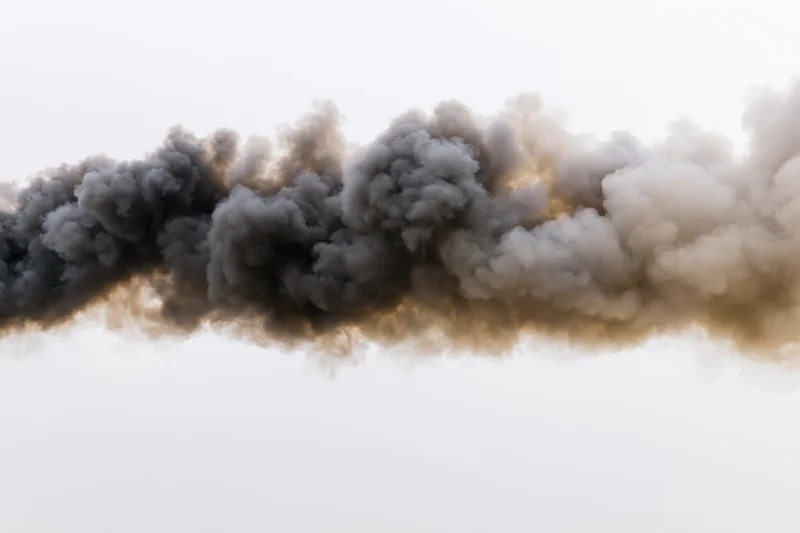 Thick dark smoke plume billowing horizontally across pale sky