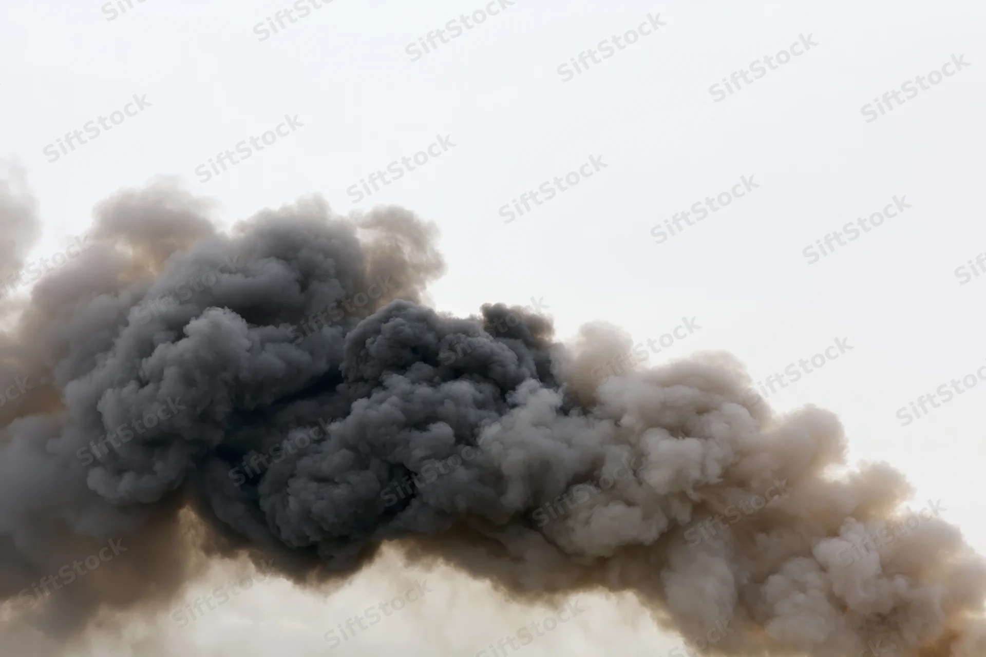 Thick dark smoke plume billowing horizontally across pale sky