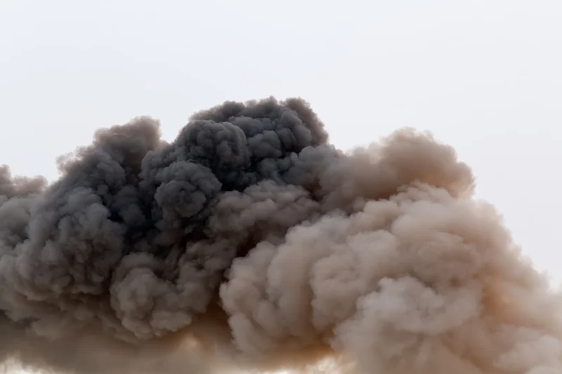 Thick dark smoke billowing horizontally across a pale sky