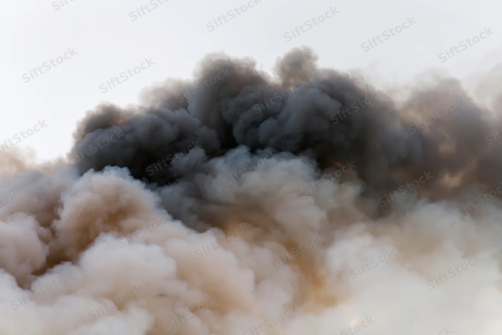 Thick dark smoke plume billowing horizontally across pale sky