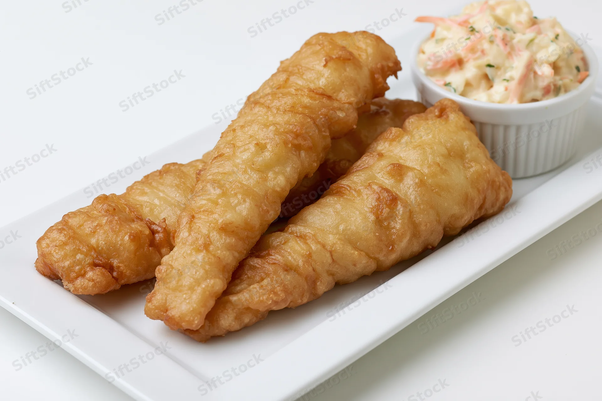 Golden-brown fried fish fillets with crispy batter on a white plate with coleslaw in a ramekin