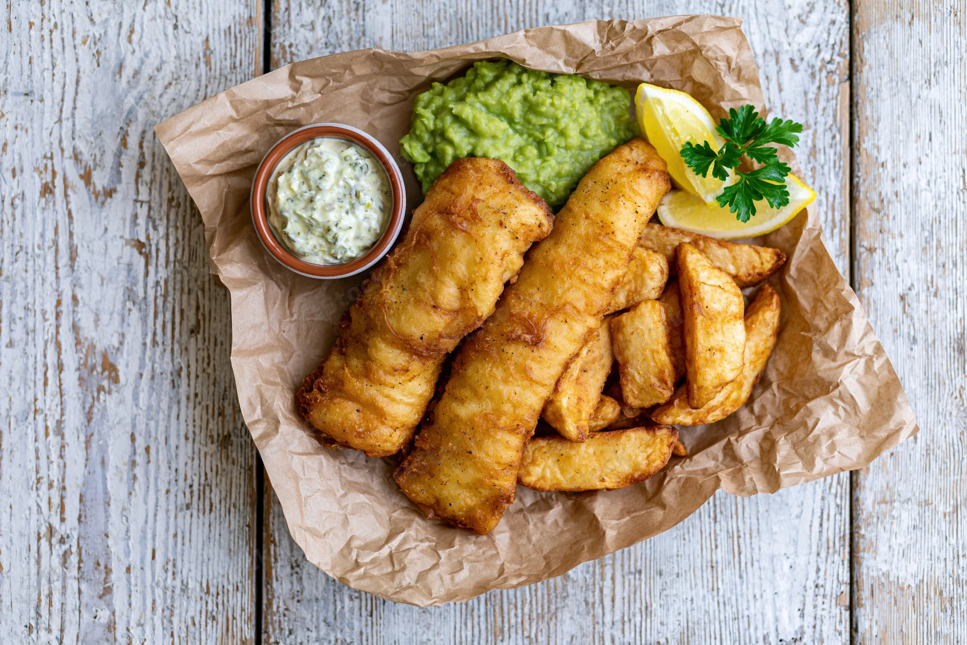 Traditional british fish and chips served on crinkled brown paper with tartar sauce and lemon garnish on a rustic wooden table