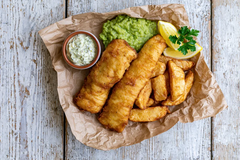 Traditional british fish and chips served on crinkled brown paper with tartar sauce and lemon garnish on a rustic wooden table