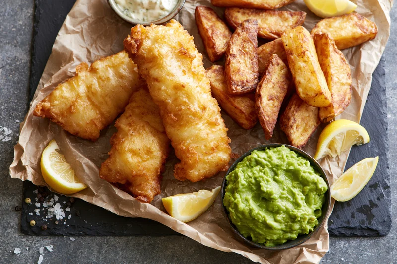 Fried fish and chips with lemon and guacamole on crumpled paper over slate plate
