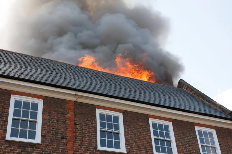 Flames erupting from the roof of a two-story brick house with white windows
