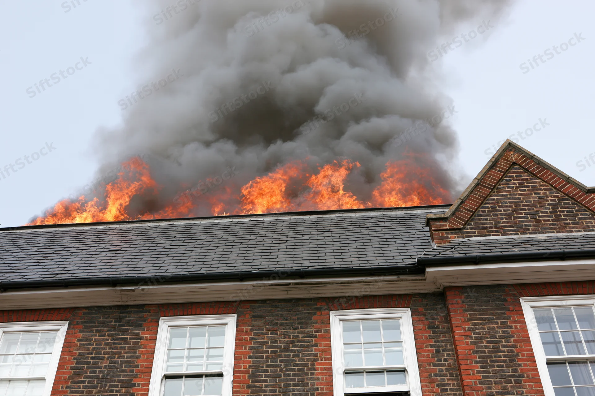 Flames engulfing the roof of a two-story brick house