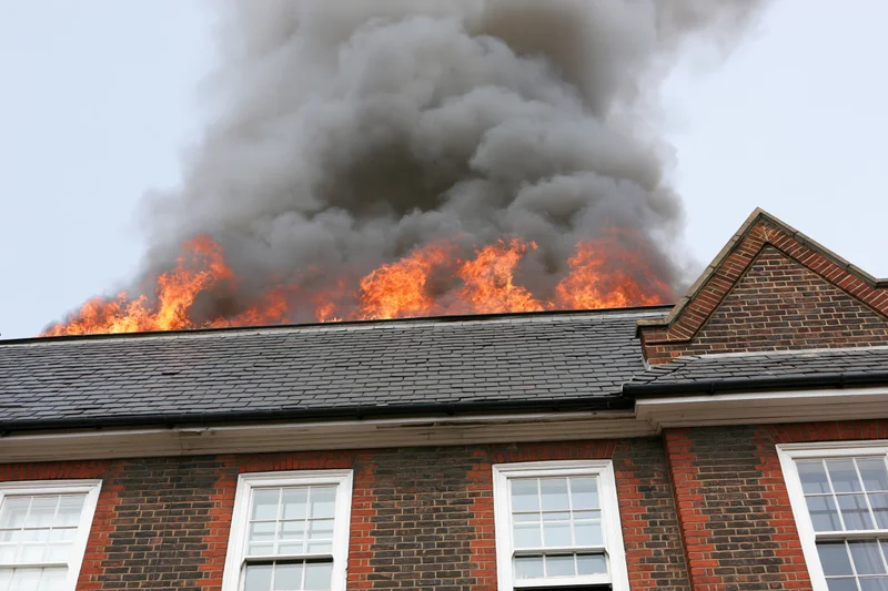 Flames engulfing the roof of a two-story brick house