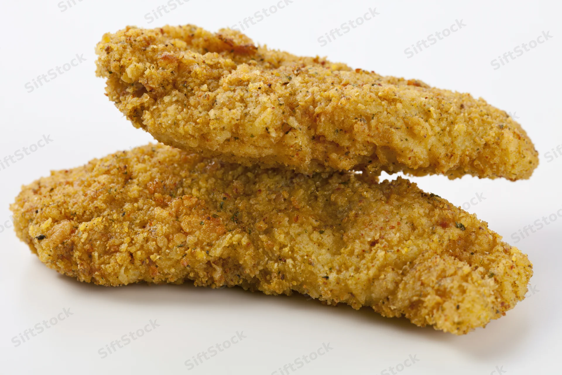 Two breaded chicken tenders stacked on a white surface