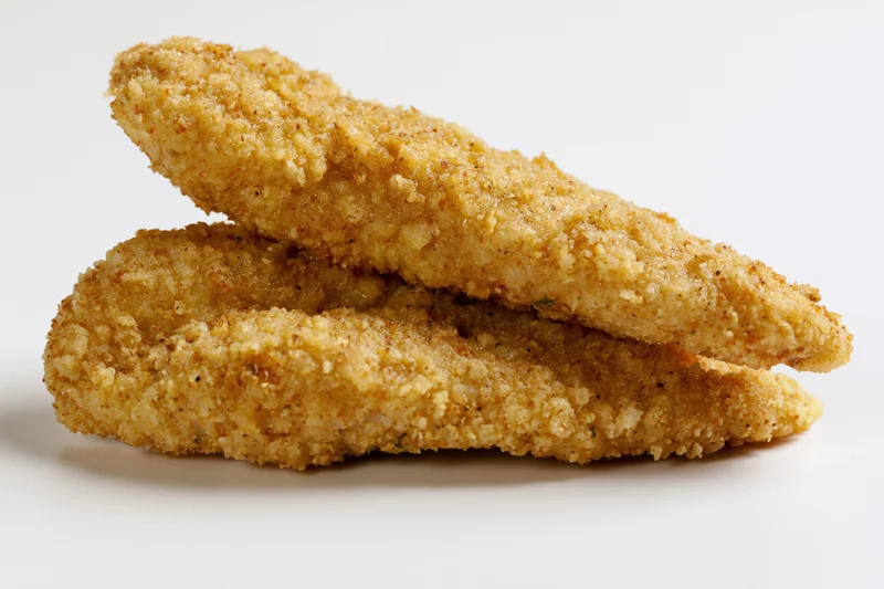 Two breaded chicken tenders stacked on a white surface