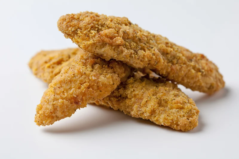 Breaded chicken tenders stacked on a white surface