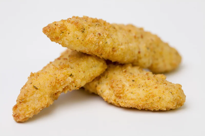 Three breaded chicken tenders stacked slightly overlapping on a white surface