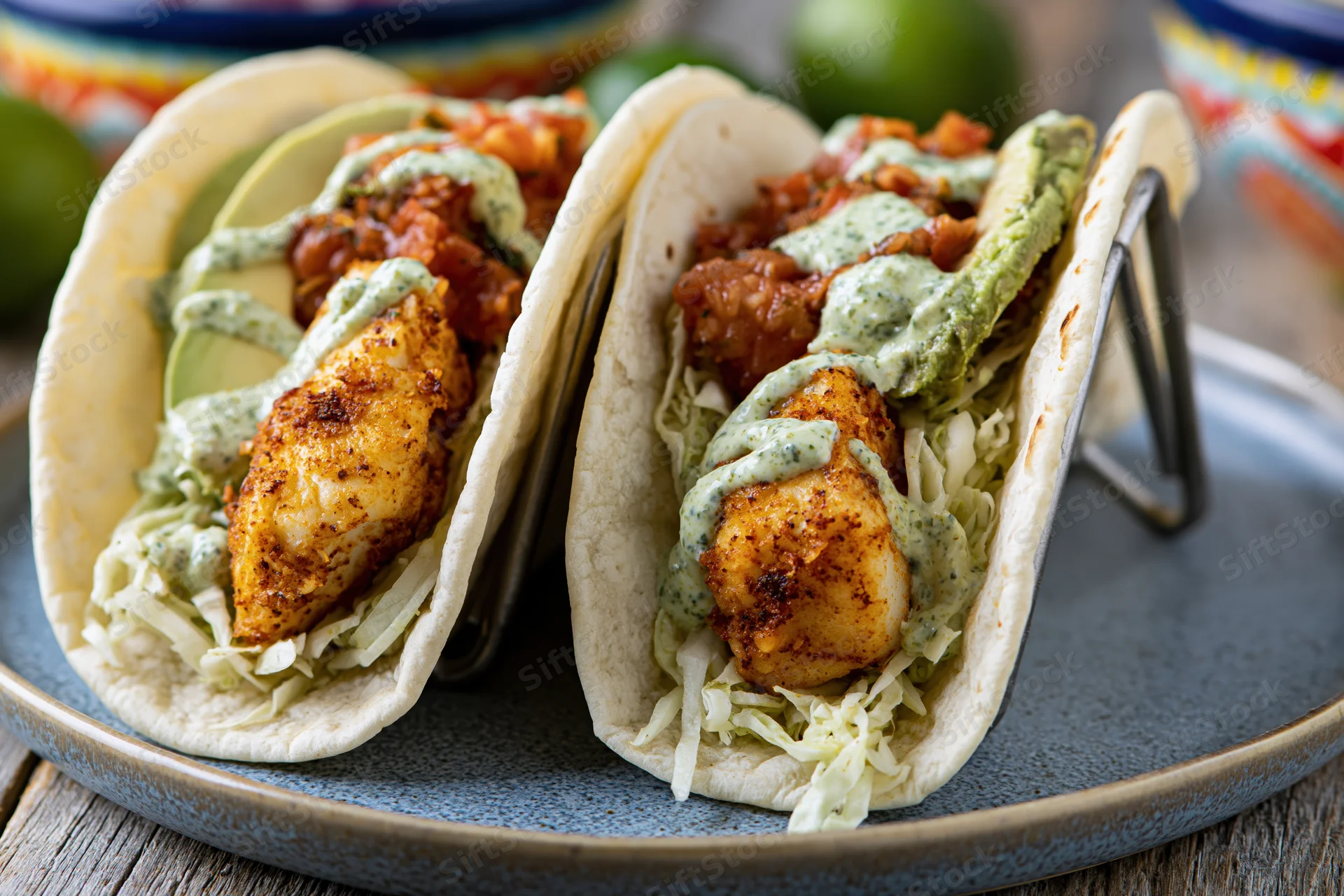 Two fish tacos in soft flour tortillas held upright in a metal stand on a blue plate