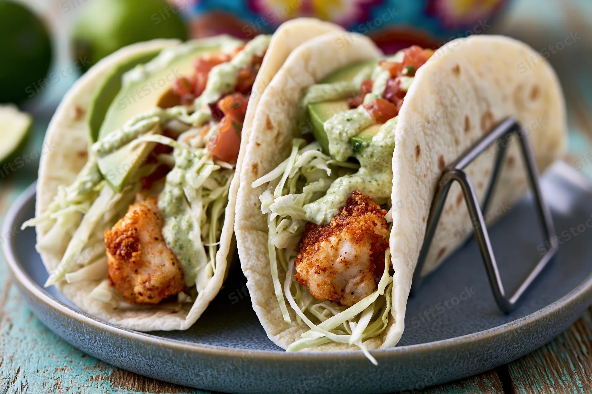 Two fish tacos in soft flour tortillas held upright on a plate with avocado, cabbage, and sauce